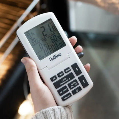 une personne tenant un Thermomètre et minuterie ChefAlarm de la marque Thermometre.fr devant un grill.