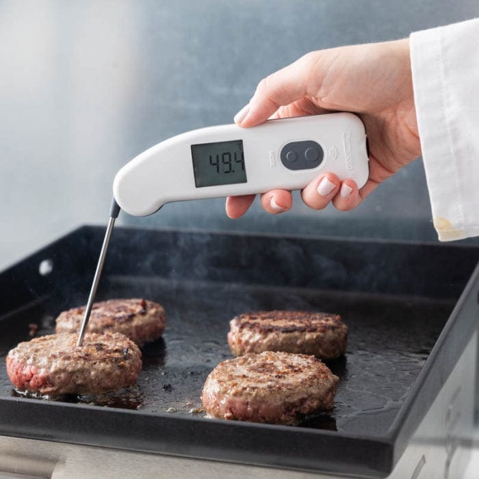 Une personne utilisant un thermomètre infrarouge Thermomètre.fr pour vérifier la température de surface des burgers.