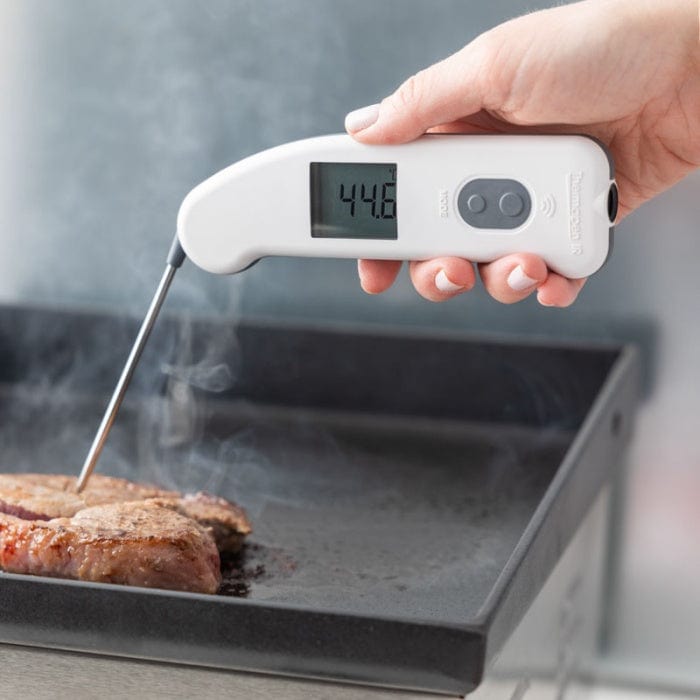 Personne utilisant un thermomètre infrarouge Thermomètre.fr pour vérifier la température de surface d'un steak.
