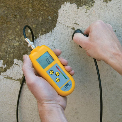 Un professionnel tenant un Humidimètre 7000 avec sonde à côté d'un mur pour mesurer la température d'un bâtiment.
