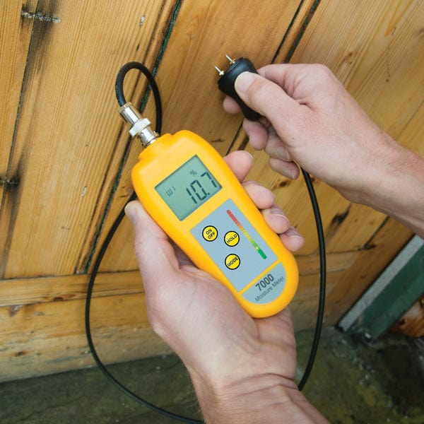 Un entrepreneur professionnel du bâtiment tenant un Humidimètre 7000 avec sonde de Thermomètre.fr devant une porte en bois tout en utilisant des sondes interchangeables.