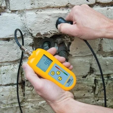 Un professionnel du bâtiment utilise l'Humidimètre 7000 avec sondes interchangeables de Thermomètre.fr pour mesurer la pression sur un mur de briques.